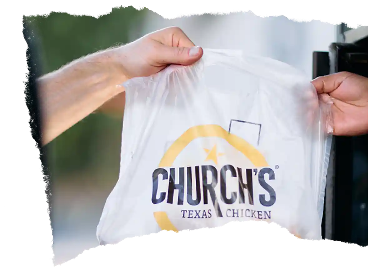 Hand passing a Church’s Texas Chicken® take-out bag to another person.